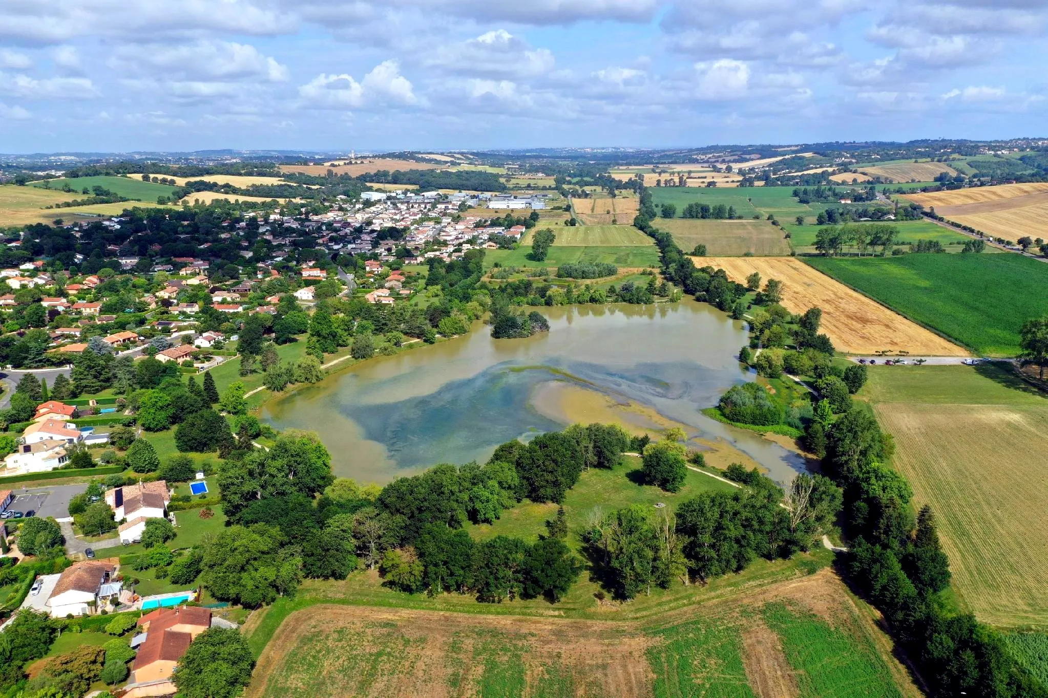 Vue aérienne du lac du Val de Saune, entre les maisons du village et les champs.